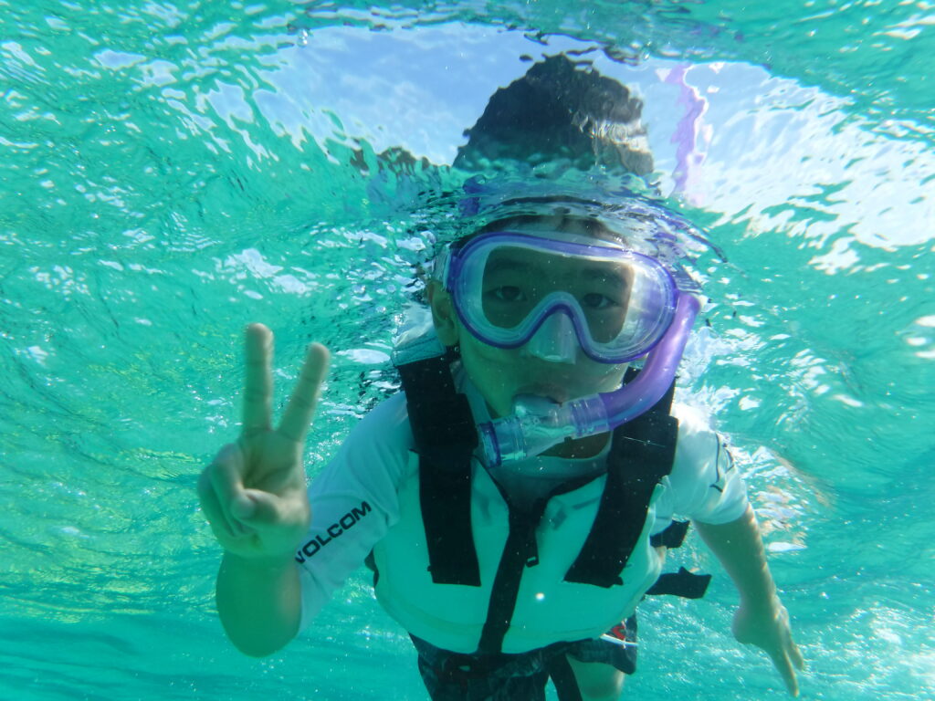 子供がピースサインでリラックスしてシュノーケリングしている様子