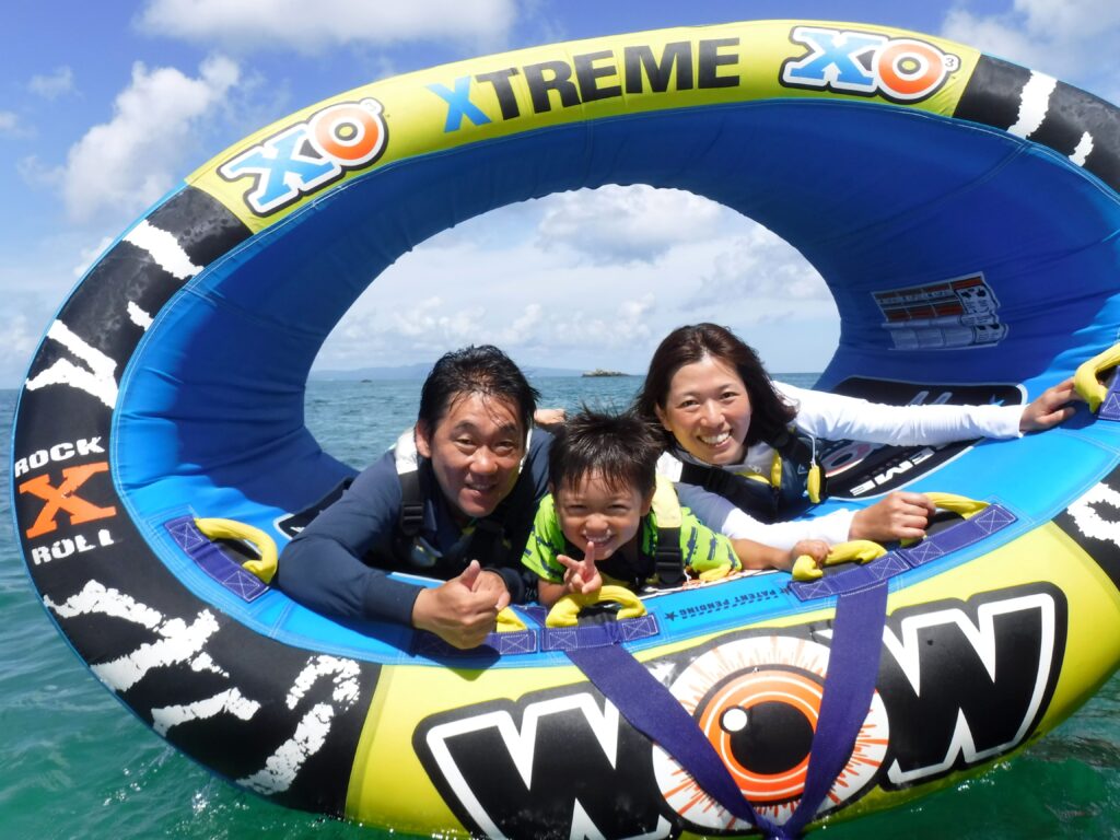 親子三人でマリンスポーツに乗っている様子。男の子は両親に挟まれてとても良い笑顔です
