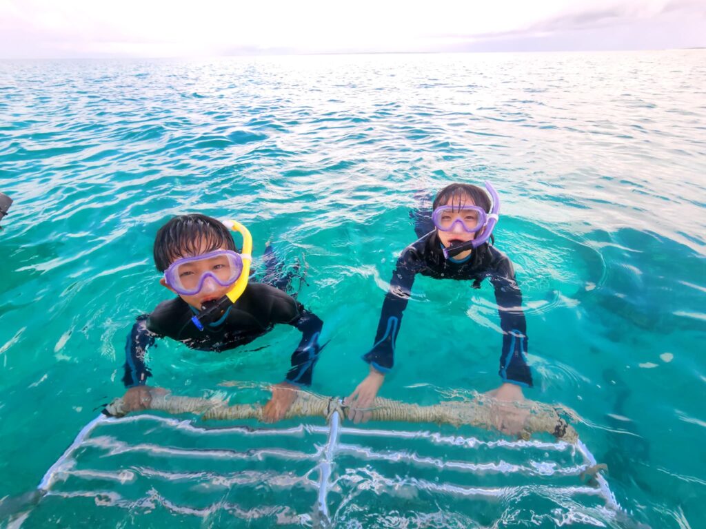2人の子供がボートの梯子に掴まってシュノーケリングの練習をしている様子