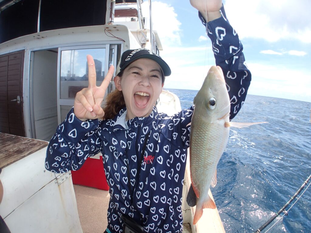 女性がクチナジ(フエフキダイ系の魚)を釣り上げてピースサインしているようす